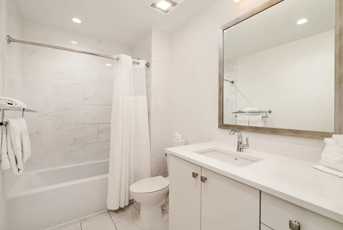 A serene, modern bathroom featuring a freestanding bathtub, a sleek sink with a wide mirror above, plush towels, and tranquil lighting. The clean lines and tasteful design create an inviting space for relaxation or getting ready for the day.