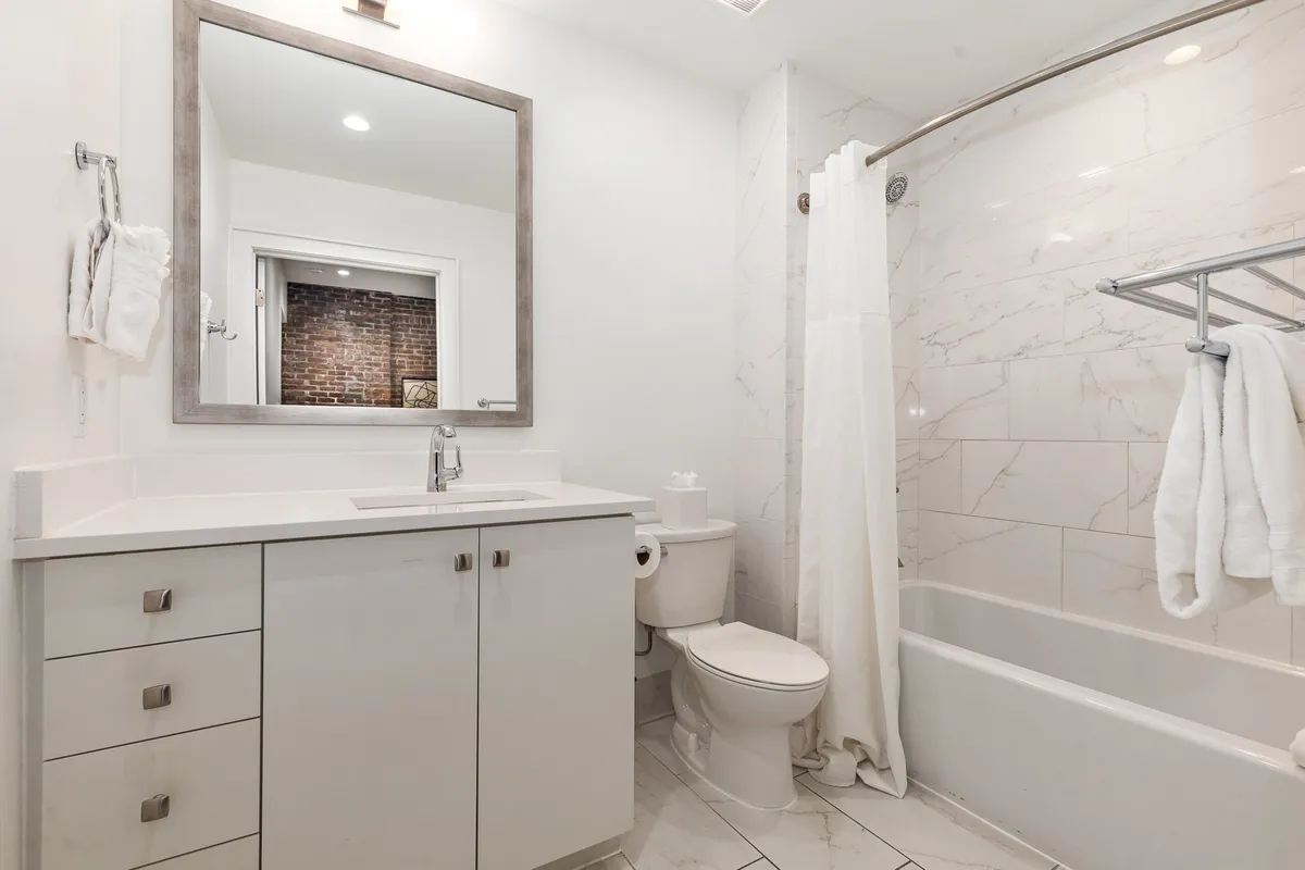 A spacious vanity area with a large mirror, modern sink, bathtub, and toilet, flooded with natural light. The space feels fresh and inviting, perfect for both quick grooming and leisurely routines.